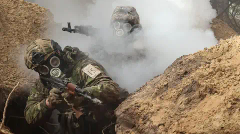 Reuters Two Ukrainian soldiers moving through a trench during a chemical weapons training drill. They both have gas masks on and one is partially-obscured by smoke.